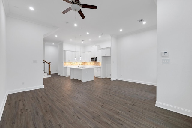 unfurnished living room featuring a ceiling fan, dark wood-style flooring, crown molding, and stairway