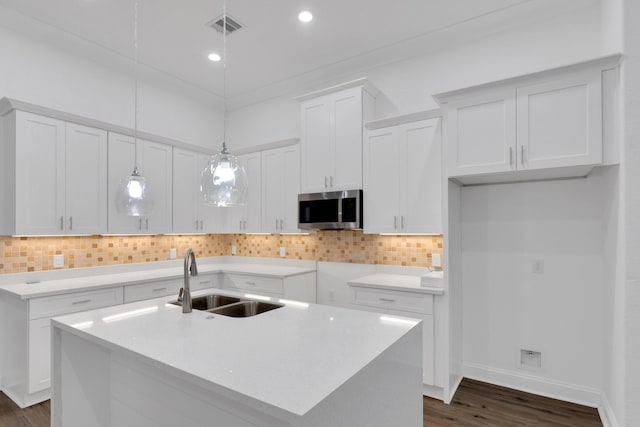 kitchen featuring visible vents, white cabinets, stainless steel microwave, a sink, and backsplash