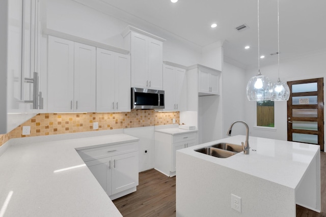 kitchen featuring a center island with sink, stainless steel microwave, visible vents, backsplash, and a sink