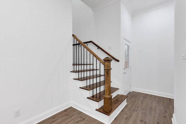 stairway with ornamental molding, wood finished floors, and baseboards