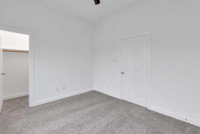 unfurnished bedroom with carpet, a walk in closet, a closet, ceiling fan, and baseboards