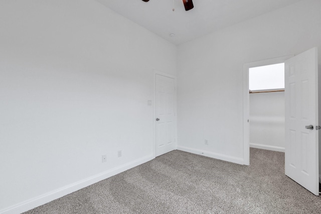 unfurnished bedroom with carpet floors, a walk in closet, a closet, a ceiling fan, and baseboards