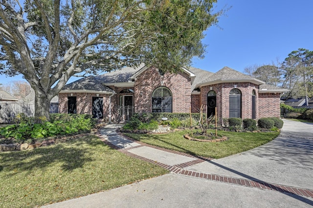 view of front facade with a shingled roof, a front lawn, and brick siding