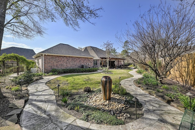 view of front facade with cooling unit, brick siding, a shingled roof, fence, and a front lawn