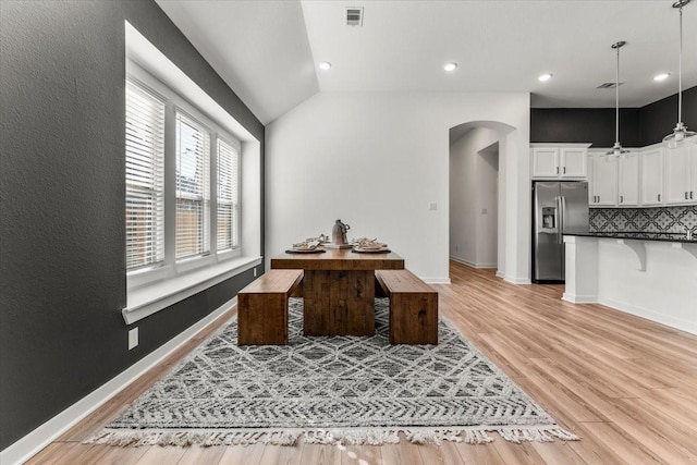 interior space featuring arched walkways, lofted ceiling, visible vents, baseboards, and light wood finished floors