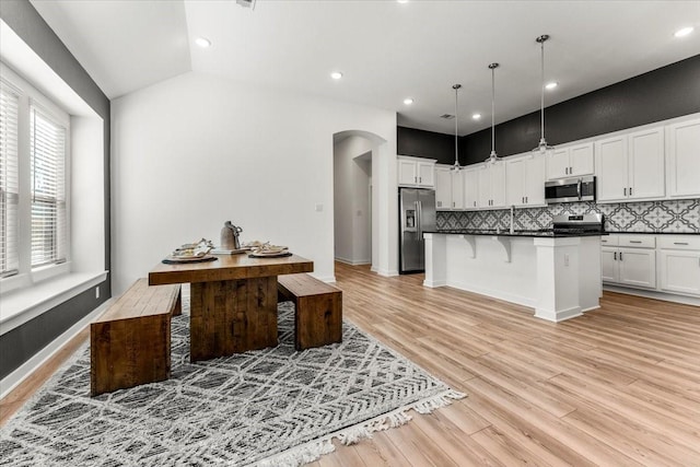 kitchen featuring a breakfast bar area, dark countertops, backsplash, appliances with stainless steel finishes, and light wood-type flooring