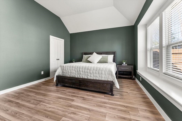 bedroom featuring lofted ceiling, a closet, baseboards, and light wood-style floors