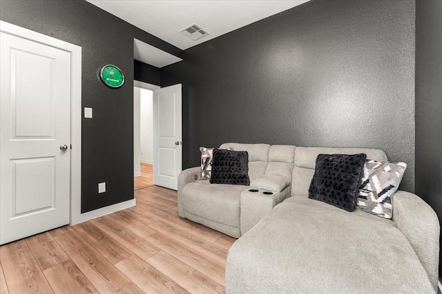 living area with baseboards, visible vents, a textured wall, and light wood finished floors