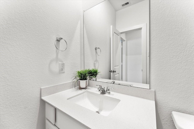 bathroom featuring visible vents, a textured wall, vanity, and toilet