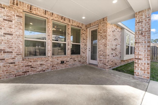 view of exterior entry featuring brick siding and a patio