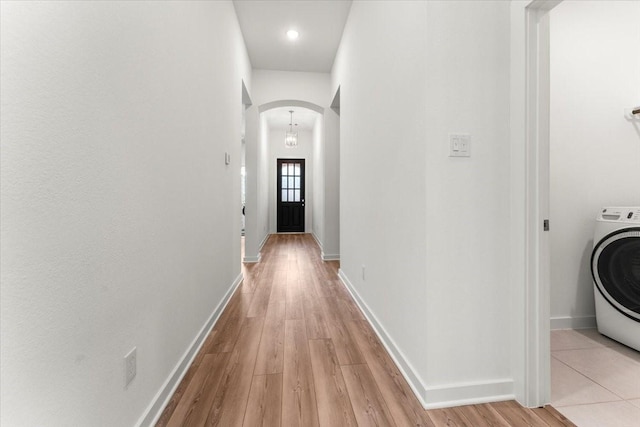 corridor with light wood finished floors, baseboards, washer / clothes dryer, and arched walkways