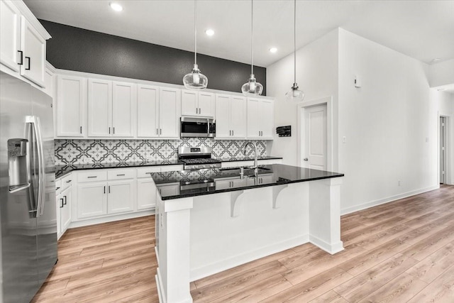 kitchen featuring tasteful backsplash, white cabinets, light wood-style flooring, appliances with stainless steel finishes, and a kitchen island with sink