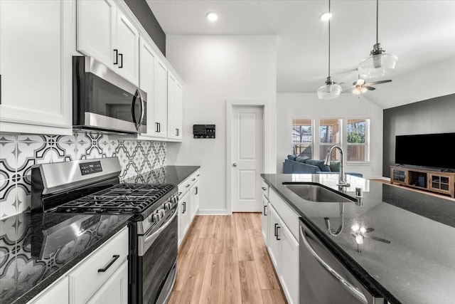 kitchen featuring dark stone counters, stainless steel appliances, light wood finished floors, and a sink