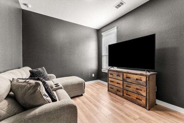 living area featuring visible vents, a textured wall, light wood-style flooring, and baseboards