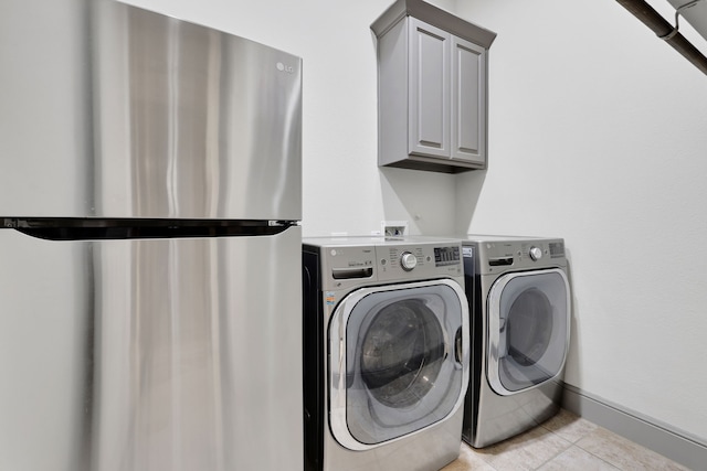 laundry room with light tile patterned floors, washing machine and dryer, cabinet space, and baseboards