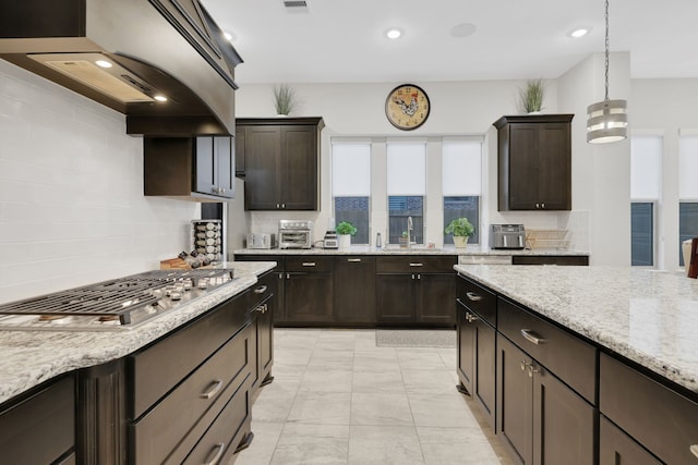 kitchen with dark brown cabinets, a sink, light stone countertops, and stainless steel gas stovetop