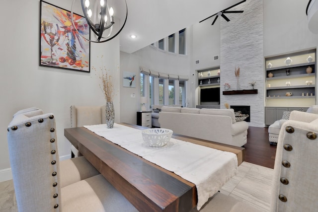 dining area with a fireplace, visible vents, a towering ceiling, baseboards, and ceiling fan with notable chandelier