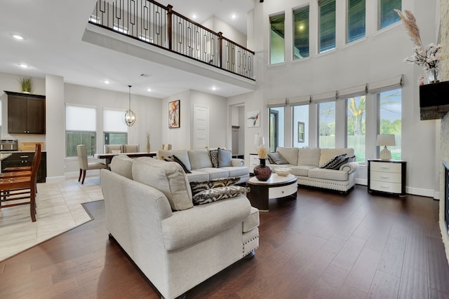 living area with baseboards, a towering ceiling, dark wood-style flooring, an inviting chandelier, and recessed lighting