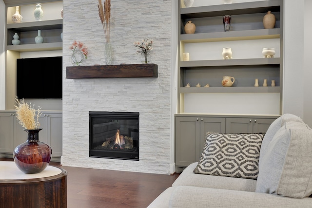 living room with a stone fireplace, wood finished floors, and built in shelves