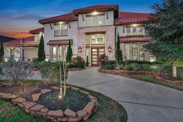 mediterranean / spanish home featuring stone siding, french doors, a tiled roof, and stucco siding