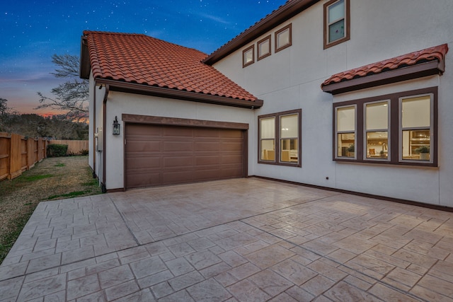 exterior space with an attached garage, a tile roof, fence, and decorative driveway