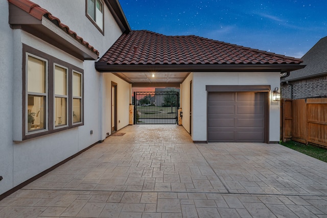 exterior space with an attached garage, fence, a tiled roof, decorative driveway, and stucco siding