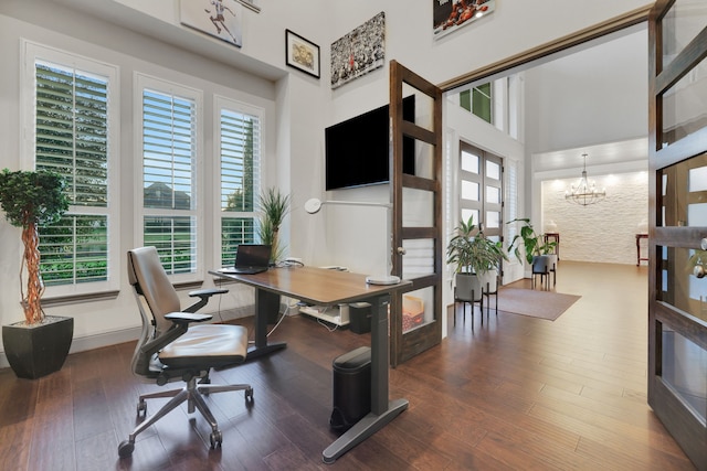 home office with a chandelier, wood finished floors, and a towering ceiling