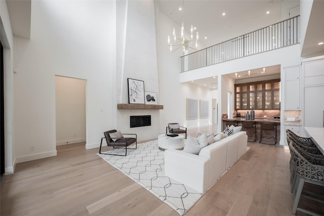 living area with a chandelier, a fireplace, a towering ceiling, baseboards, and light wood-style floors