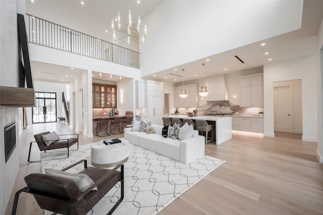 living room with a high ceiling, light wood-style floors, a fireplace, a chandelier, and recessed lighting