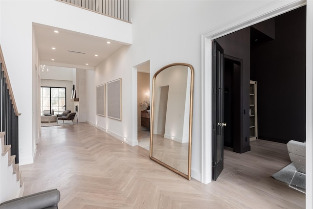 hallway with baseboards, stairs, a high ceiling, and recessed lighting