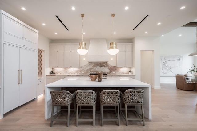 kitchen with light countertops, a large island with sink, light wood-style floors, premium range hood, and white cabinetry