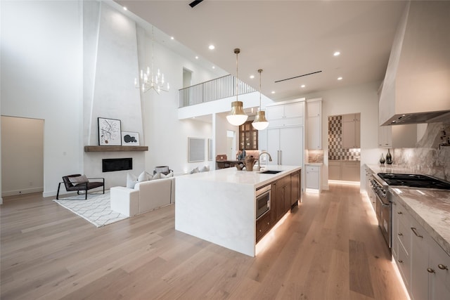 kitchen with a large fireplace, light wood finished floors, decorative backsplash, custom range hood, and a sink