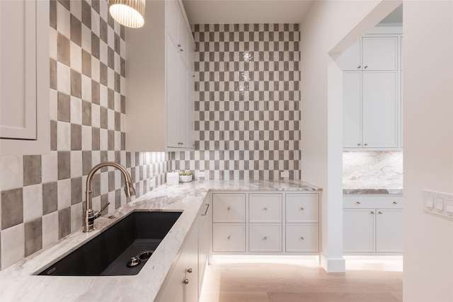 kitchen featuring white cabinetry, light stone counters, and a sink