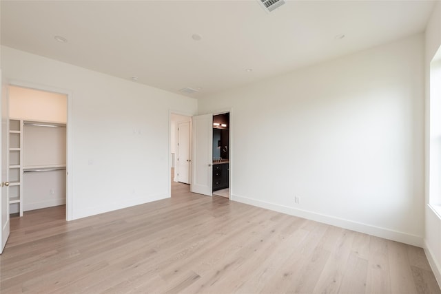 unfurnished bedroom with light wood-type flooring, visible vents, a spacious closet, and baseboards