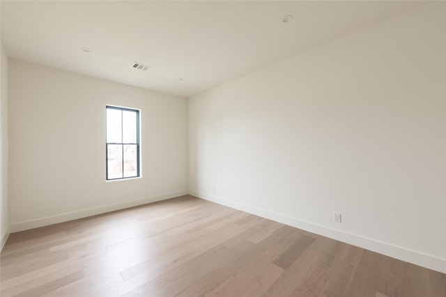 empty room with light wood finished floors, visible vents, and baseboards