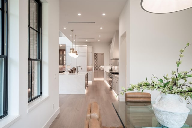 corridor featuring light wood-type flooring, a sink, and recessed lighting