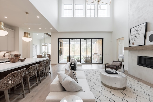 living area with recessed lighting, a high ceiling, baseboards, light wood-type flooring, and a glass covered fireplace