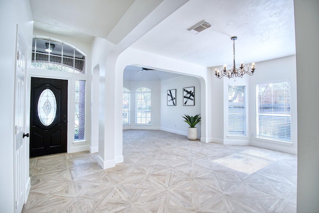 foyer featuring an inviting chandelier, baseboards, visible vents, and arched walkways