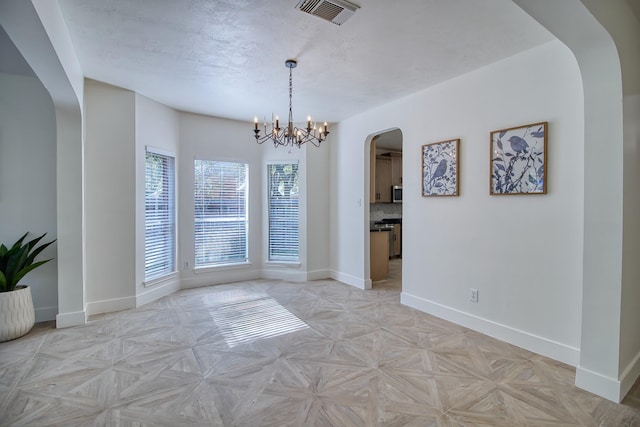 unfurnished dining area featuring baseboards, visible vents, arched walkways, a textured ceiling, and a chandelier