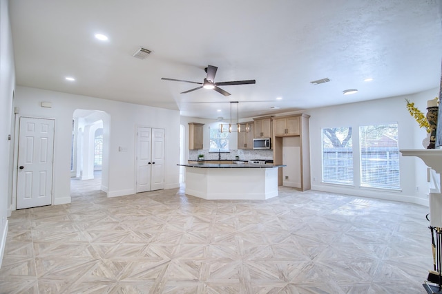 kitchen featuring arched walkways, stainless steel microwave, dark countertops, and visible vents