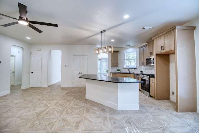 kitchen with arched walkways, a sink, appliances with stainless steel finishes, tasteful backsplash, and dark countertops