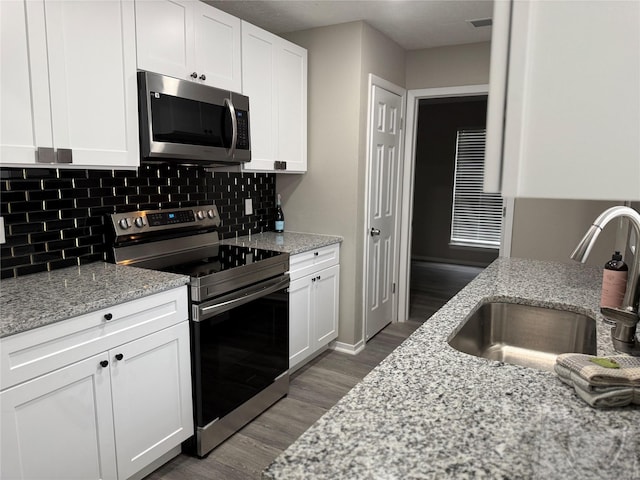 kitchen with backsplash, appliances with stainless steel finishes, white cabinetry, a sink, and wood finished floors