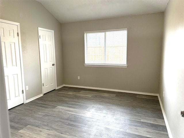 empty room featuring vaulted ceiling, wood finished floors, and baseboards