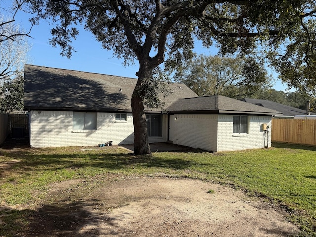 back of house with a yard, roof with shingles, fence, and brick siding