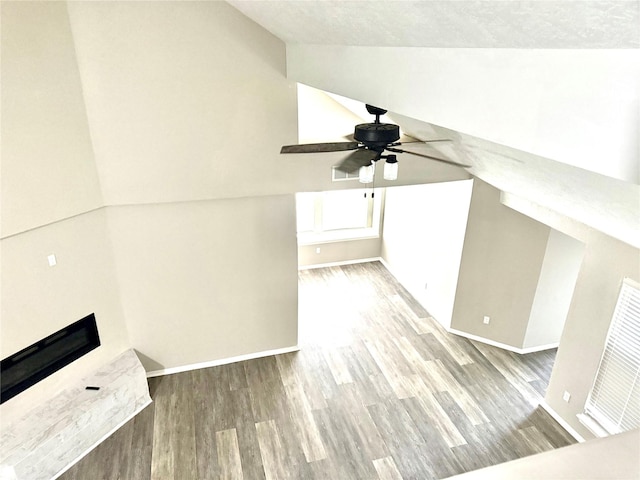 interior space featuring lofted ceiling, ceiling fan, a fireplace, wood finished floors, and baseboards