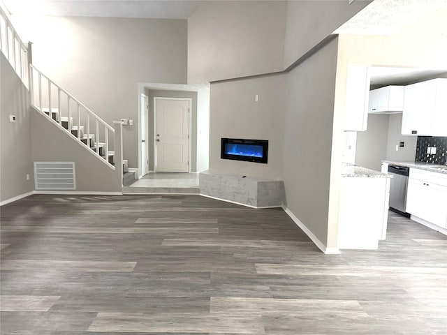 unfurnished living room with visible vents, a glass covered fireplace, a towering ceiling, light wood-style flooring, and stairs