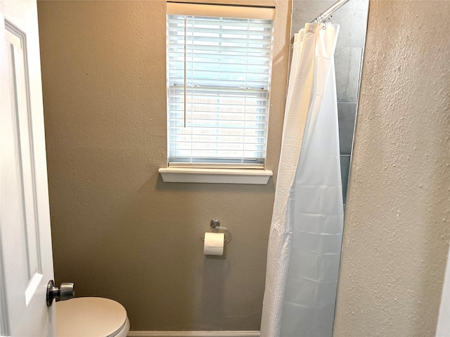 bathroom with toilet, baseboards, a shower with shower curtain, and a textured wall