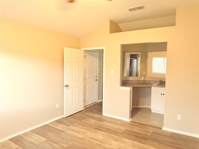 unfurnished bedroom featuring baseboards, visible vents, ensuite bathroom, vaulted ceiling, and light wood-style floors