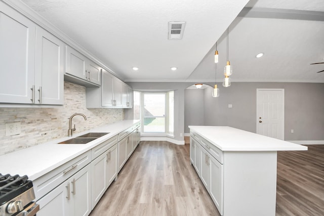 kitchen featuring a sink, visible vents, light countertops, decorative backsplash, and crown molding