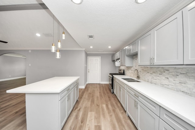 kitchen with arched walkways, visible vents, decorative backsplash, stainless steel range with gas cooktop, and a sink